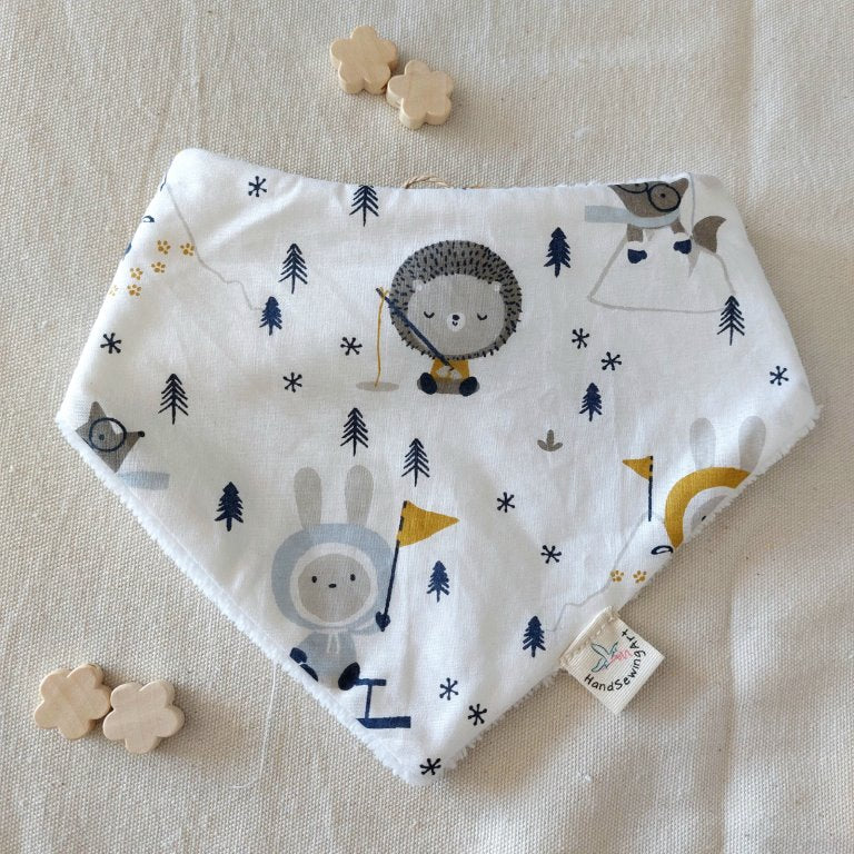 Bandana forma triangular, en fondo blanco estampado motivos nieve, esquimales, uno pescando otro sujetando banderola, huellas animales, zorrito con bufanda encondido, pinos pequeños repartidos. 