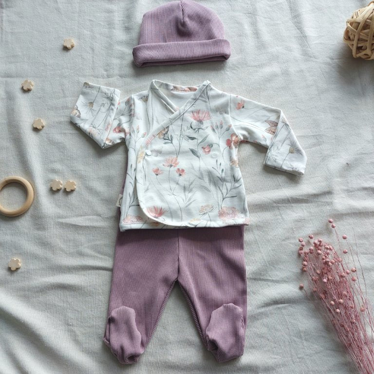 Conjunto de recién nacido, compuesto por camisa de cierre en el lateral de la barriga, estampado de ramilletes de flores en fondo blanco. Completado con gorro y polainas de color lila.