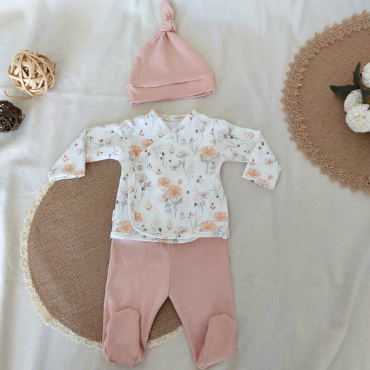 Conjunto de recién nacido, compuesto por camisa con cierre en el lateral de la barriga, con estampado de amapolas anaranjadas y claras sobre fondo blanco. Completado con polainas y gorro de color rosa