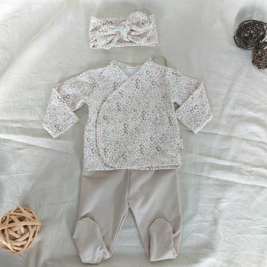 Conjunto de recién nacido, compuesto por camisa con cierre en el lateral de la barriga de estampado de animal-print. Completado con diadema del mismo estampado y polainas de color beige.