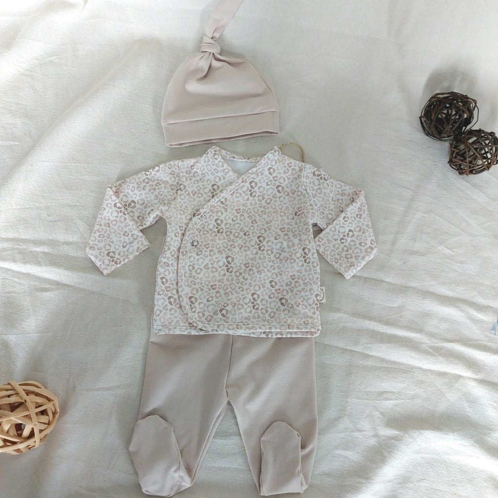 Conjunto de recién nacido, compuesto por camisa con cierre en el lateral de la barriga de estampado de animal-print. Completado con gorro de un nudo y polainas de color beige.
