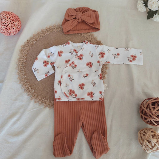 Conjunto de recién nacido, compuesto por camisa con cierre en el lateral de la barriga, con estampado de flores canela sobre fondo blanco. Completado con polainas y gorro-diadema de color marrón.