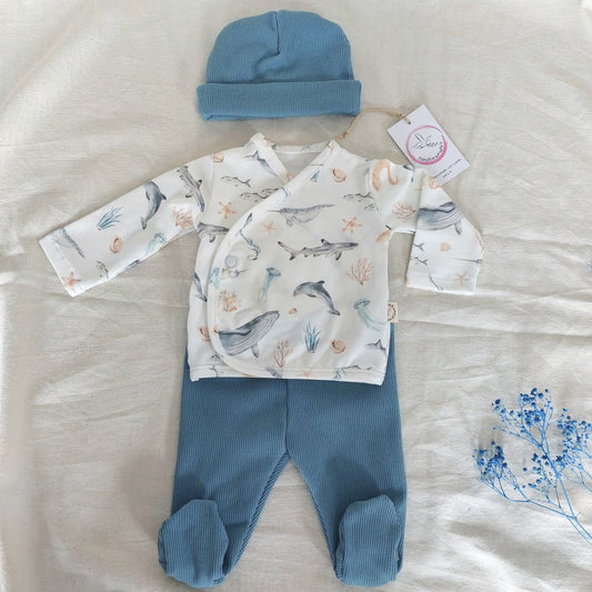 Conjunto de recién nacido, compuesto por camisa con cierre en el lateral de la barriga, estampado de fauna marina en fondo blanco. Completado con polainas y gorro redondo de color azul marino.