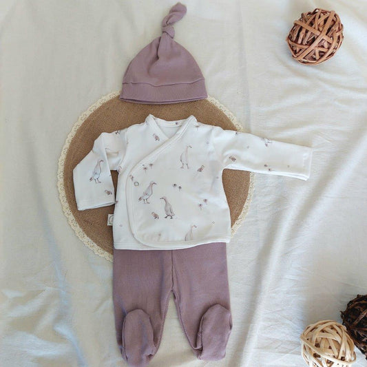 Conjunto de recién nacido, compuesto por camisa con cierre en el lateral de la barriga, estampado de ocas sobre fondo blanco. Completado con polainas y gorro de color lila.