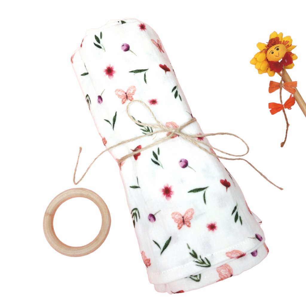 Mantita de Muselina, enrollada atada con un lazo de hilo de yute. El estampado es de mariposas de color rosa entre florecillas y ramas sobre mullido blanco 