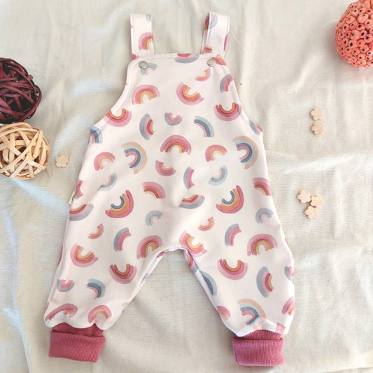 Peto para bebé, visto de frente con bonito estampado de arcoíris en fondo rosa, con puños de tobillo también rosa