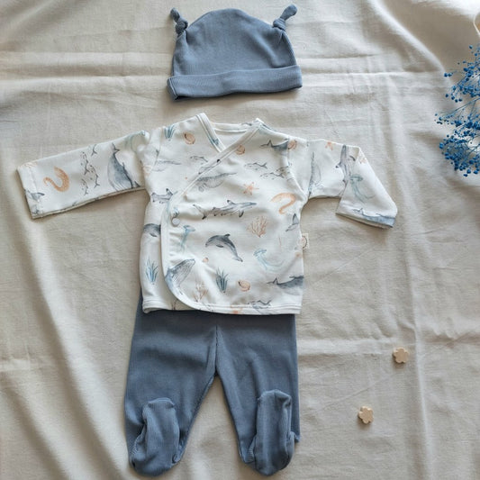 Conjunto de recién nacido, compuesto por camisa de cierre en el lateral de la barriga, estampado de fauna oceánica en fondo blanco. Completado con polainas y gorro de color azul.