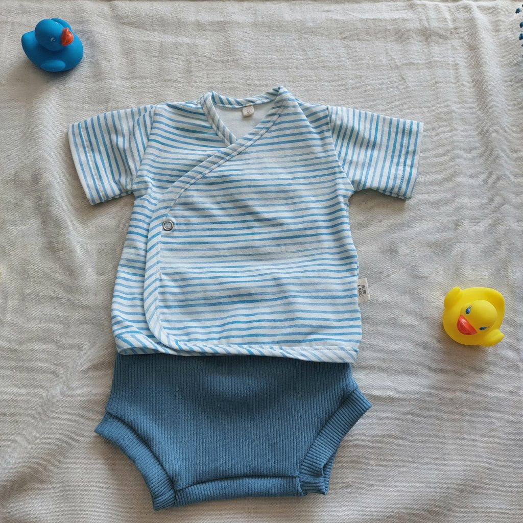 Conjunto de recién nacido, compuesto por camisa de manga corta con cierre en el lateral de la barriga de rayitas celestes y blancas. Completado con pantaloncitos cortos de color celeste.
